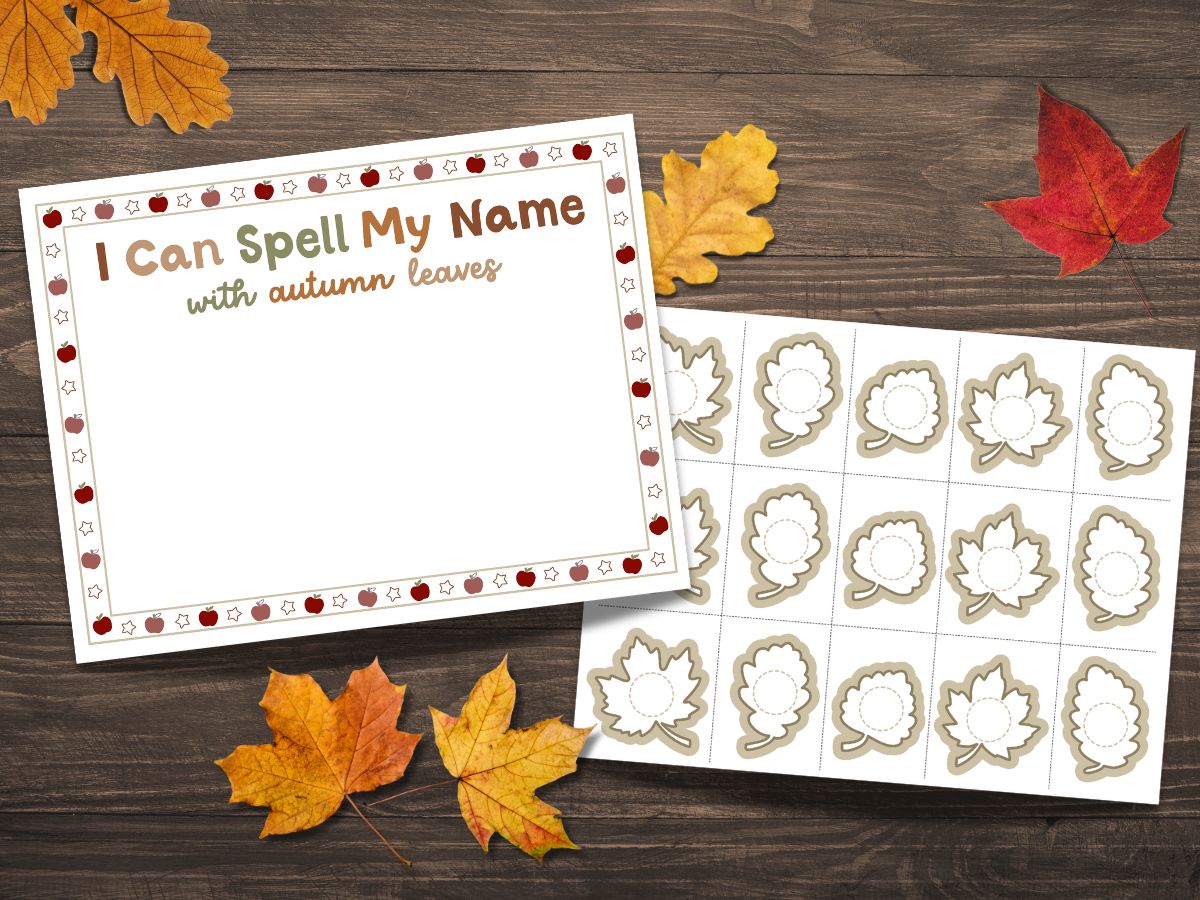Two printed pages lie on a dark wood table with fall leaves around it. One page reads 'I can spell my name with autumn leaves' and the other has a page of printable leaves to write letters on.