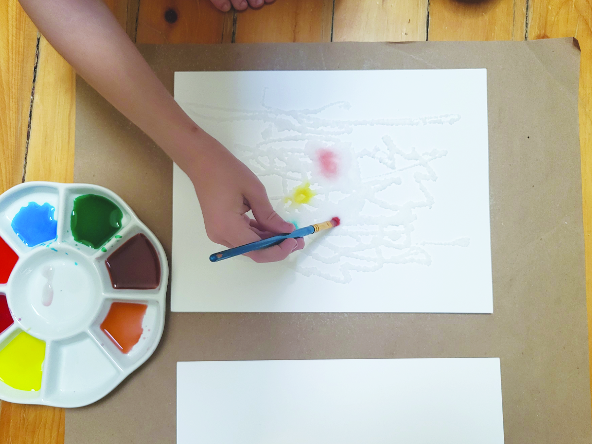 A child adds paint to their salt art project. 