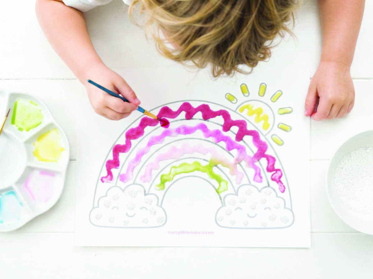 A child paints a rainbow salt art picture.
