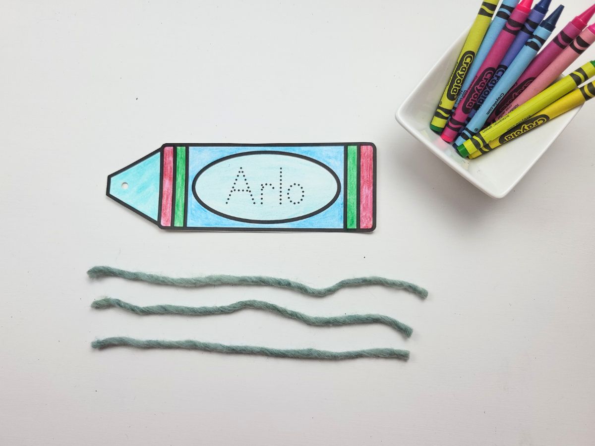 3 strands of yarn beside the crayon bookmark cutout. 