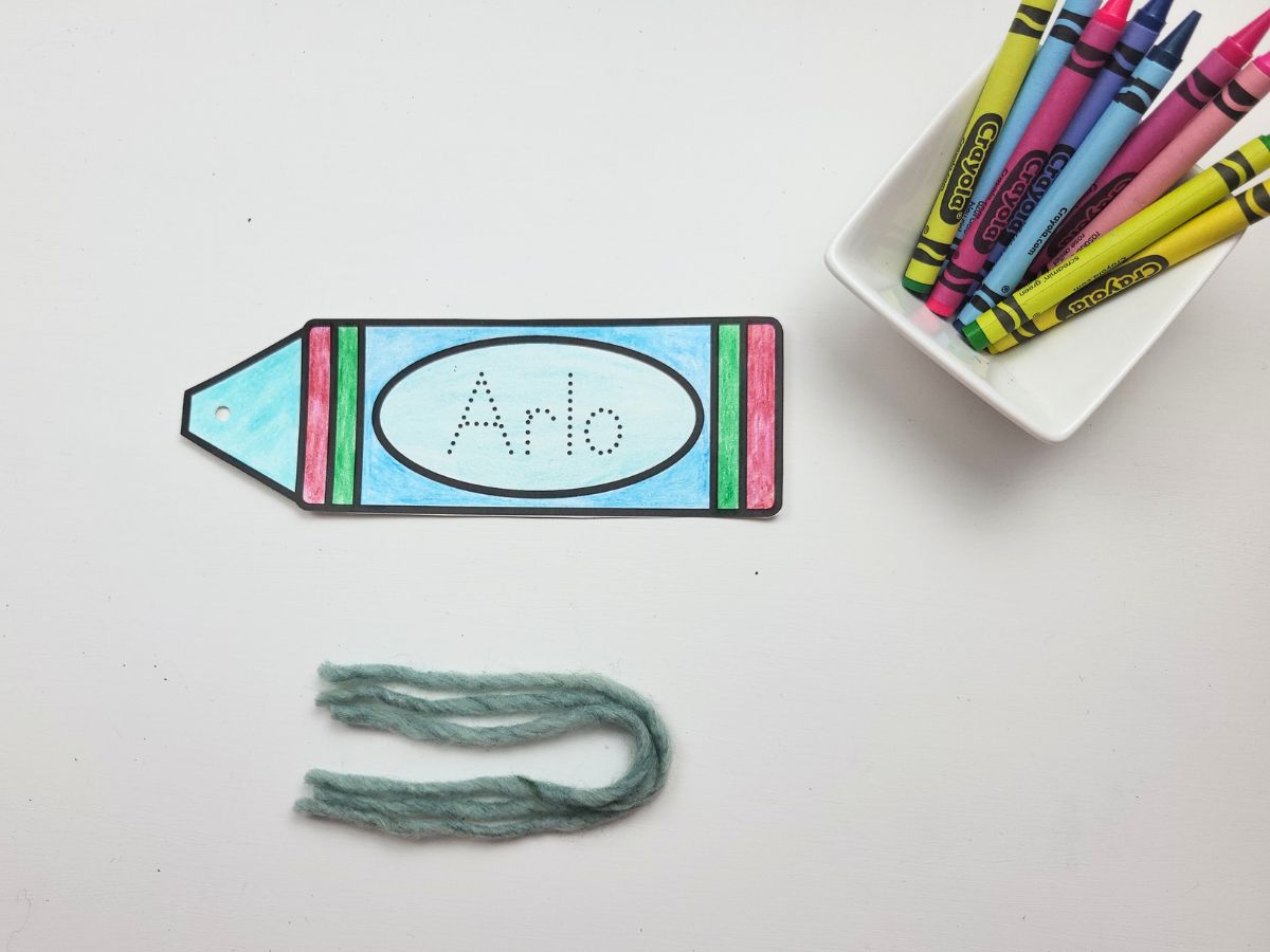3 strands of yarn beside the crayon bookmark cutout.