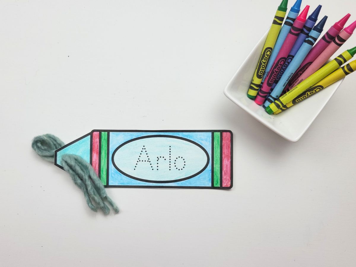 3 strands of yarn being pulled through the hole in the crayon bookmark cutout. 