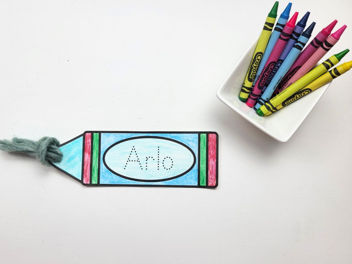 3 strands of yarn being pulled through the hole in the crayon bookmark cutout.