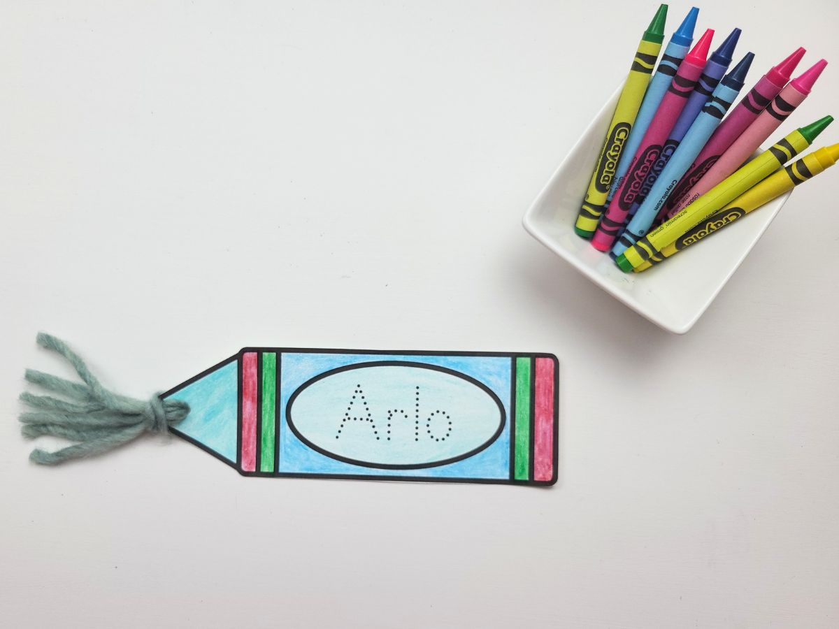 Completed crayon name bookmark beside a small container of crayons. 