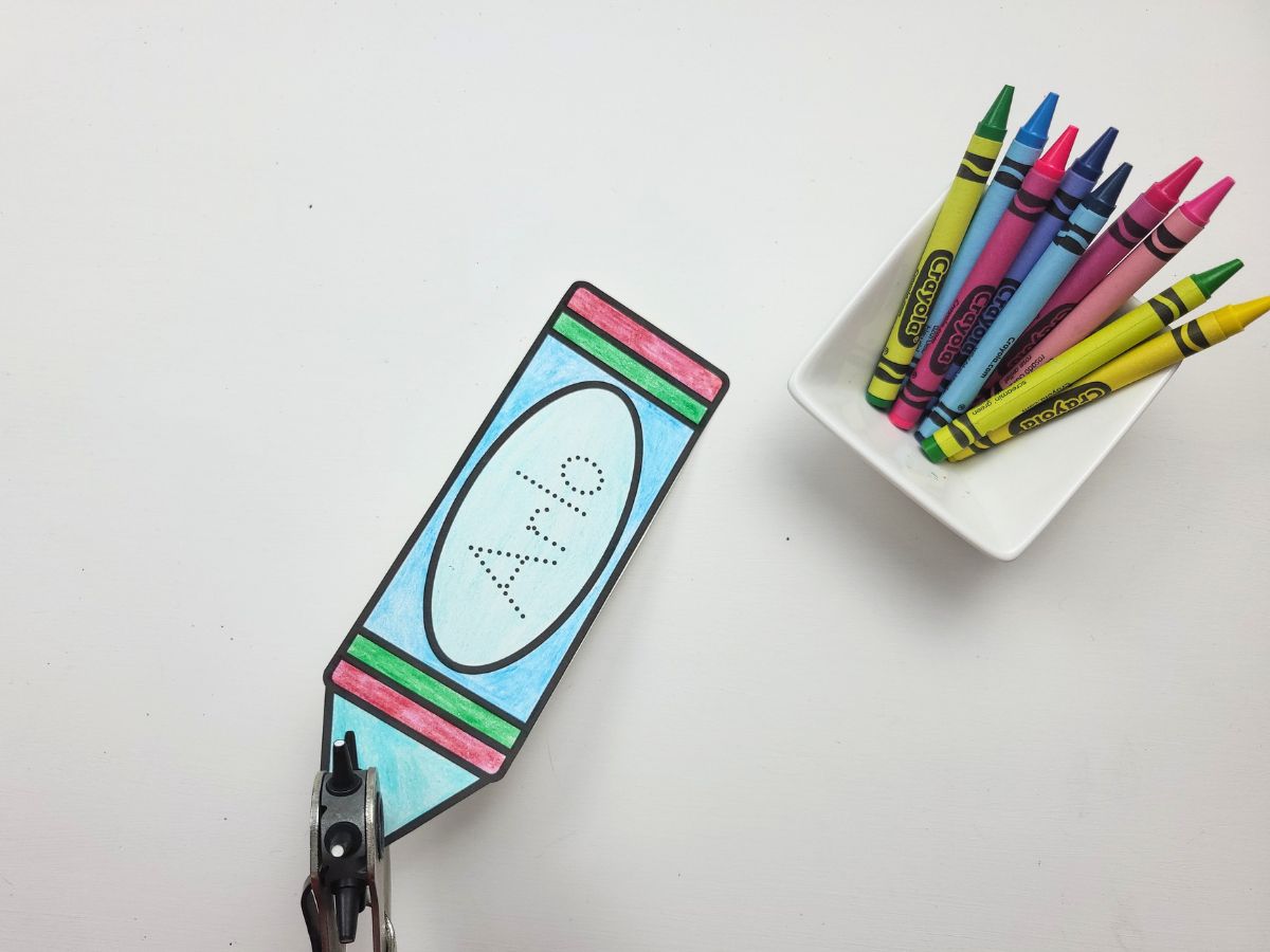 Using a hole punch to punch a hole in the top of the crayon bookmark. 